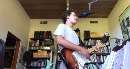 Eli Brown in a white t-shirt playing guitar.